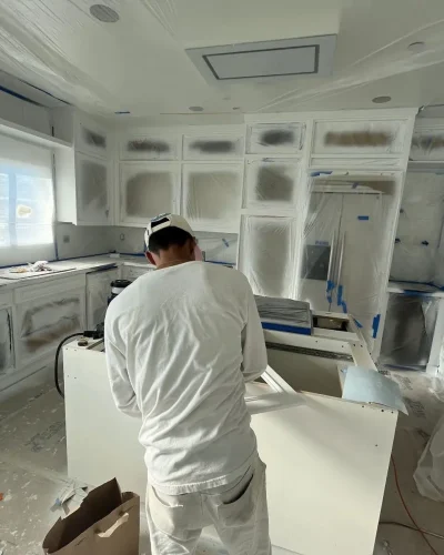 Painter spraying kitchen cabinets with surfaces masked